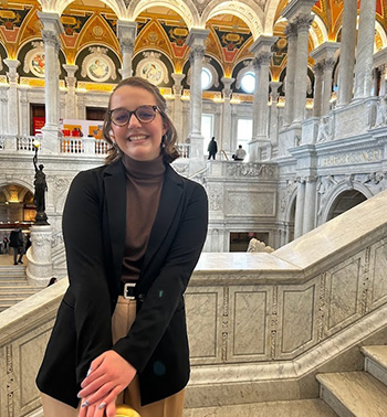 Natalie Webster smiles under an intricately designed, historical ceiling of a D.C. building