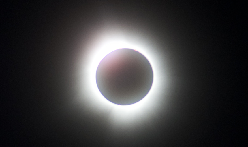 The moon eclipses the sun to near totality, leaving only a ring of light visible, while clouds cluster around the edges of the image.