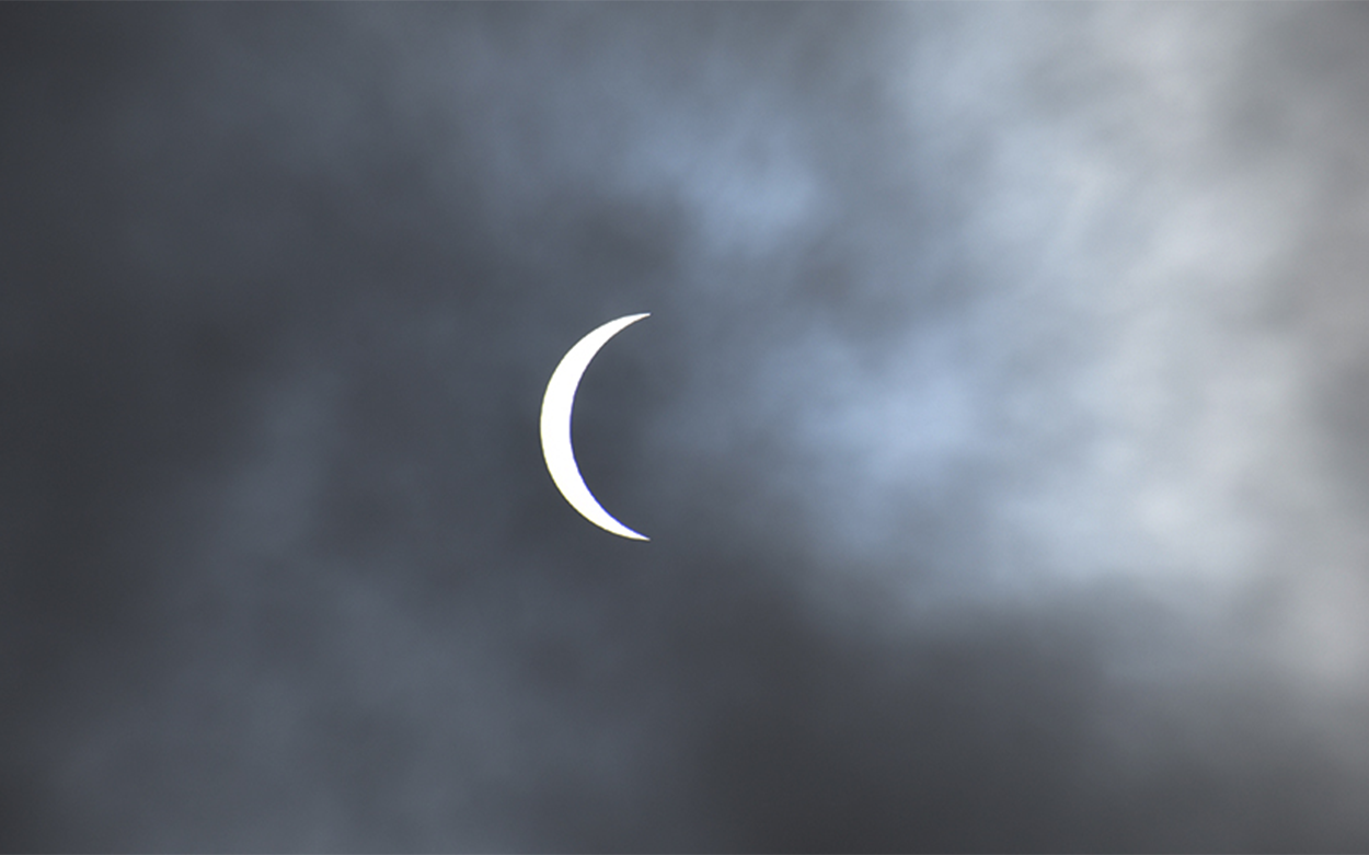 Crescent sun shows through the clouds during the solar eclipse