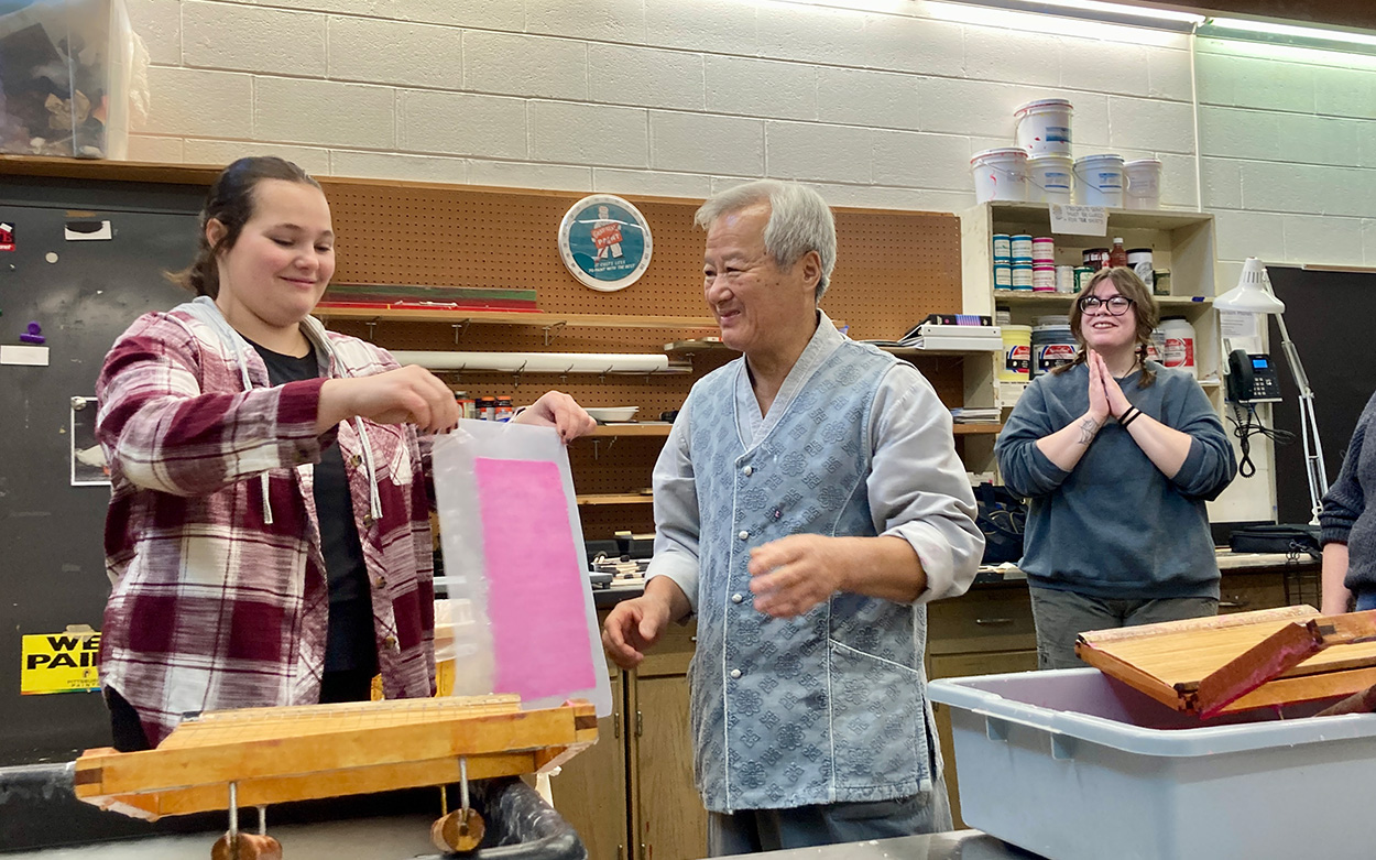 Man guiding a student through he process of making paper.