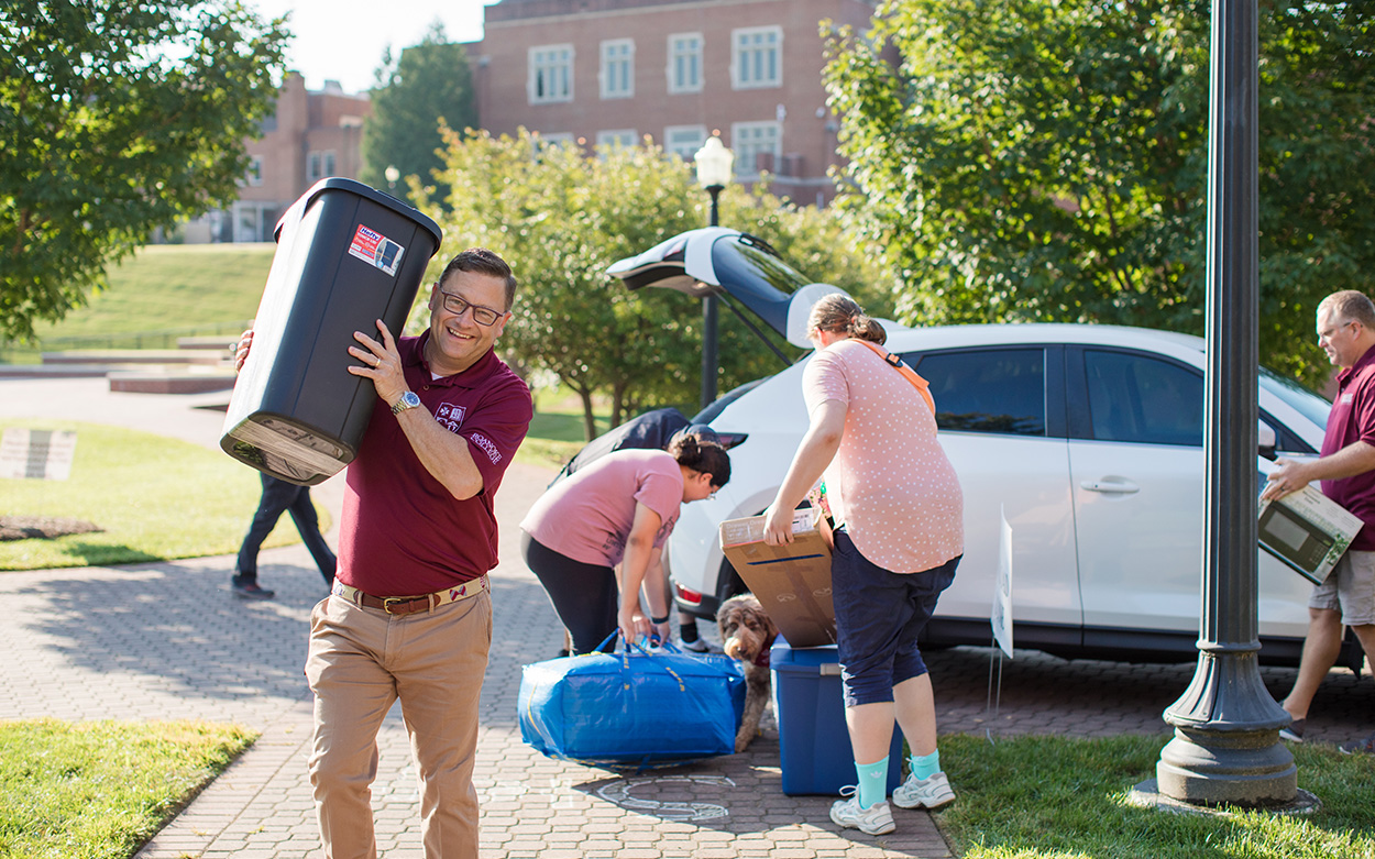 President Shushok smiles while helping a new student carry things into their residence hall