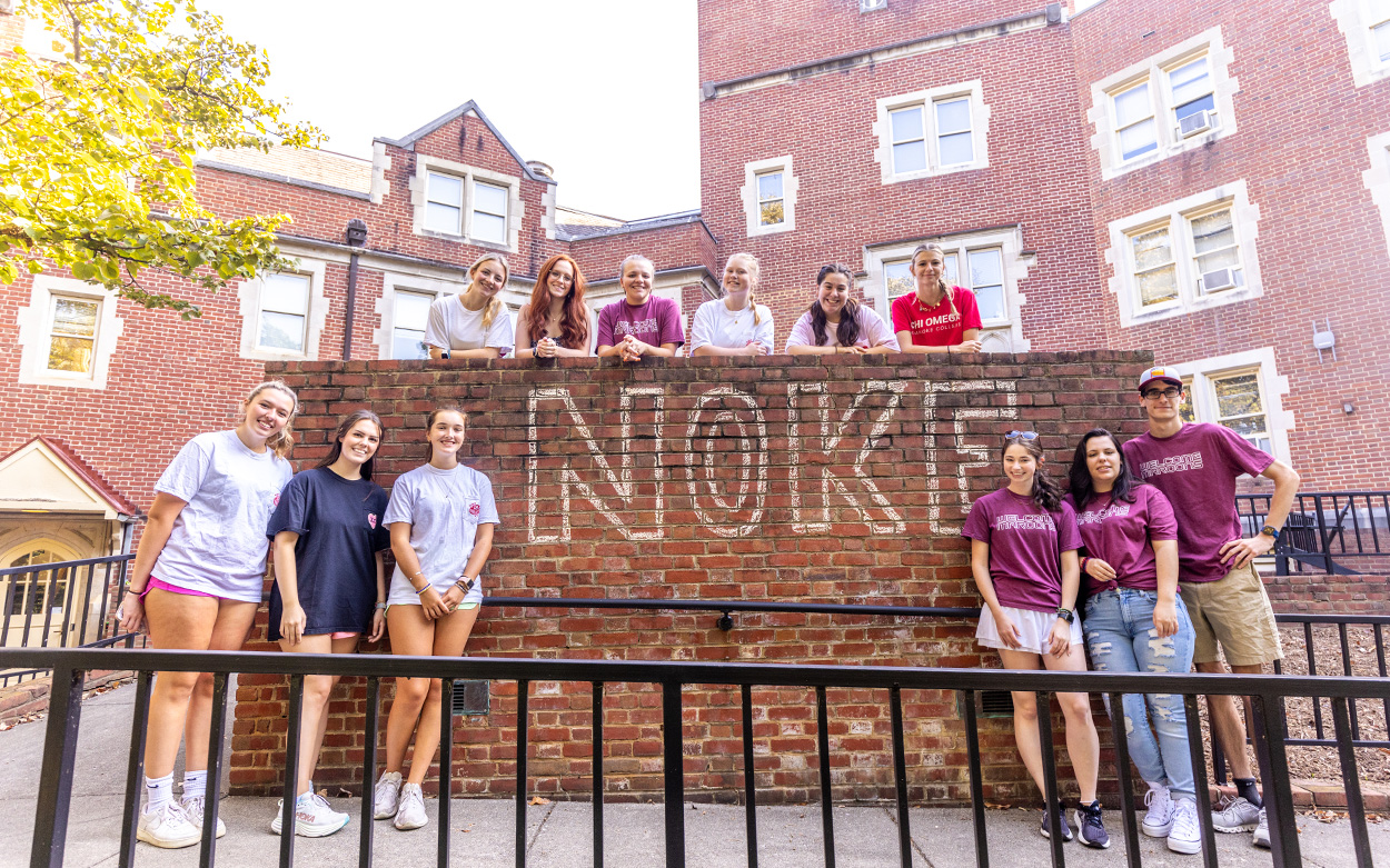 Student volunteers smile for a photo next to a wall with the word NOKE written on it in large chalk letters