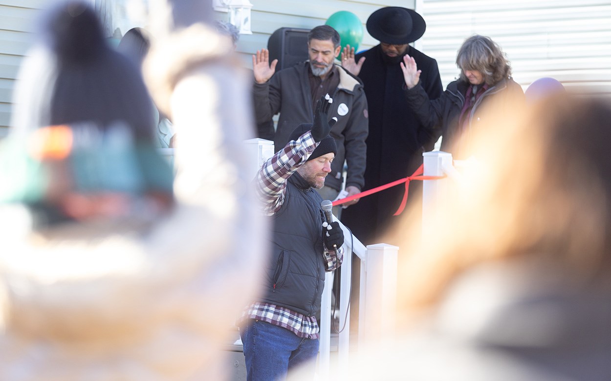 People gathered in a backyard lift their hands and bow their heads during a prayer of blessing.