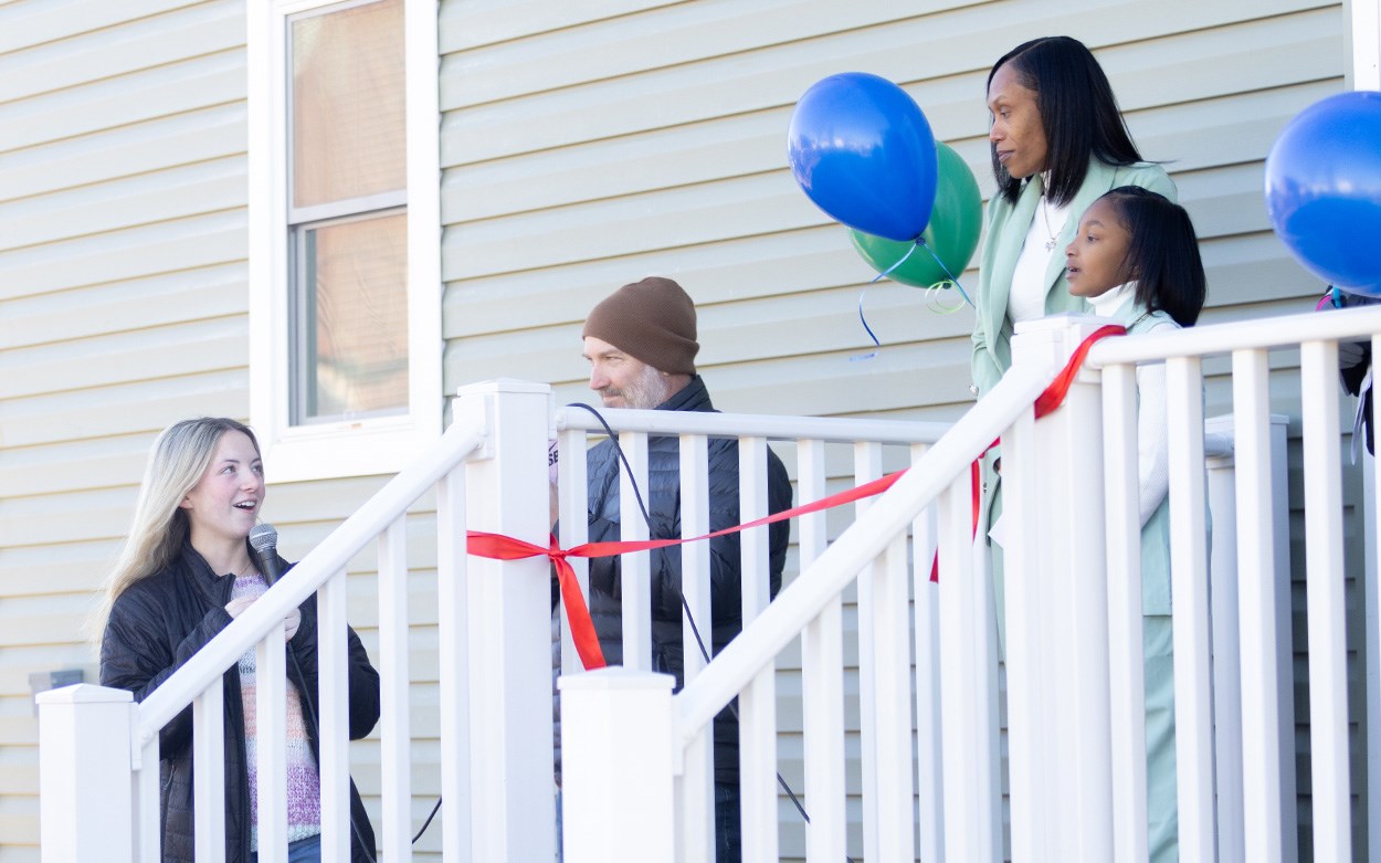 Maple Landis-Browne smiles while looking up at the Hunt family, who are standing on the new home's back porch.