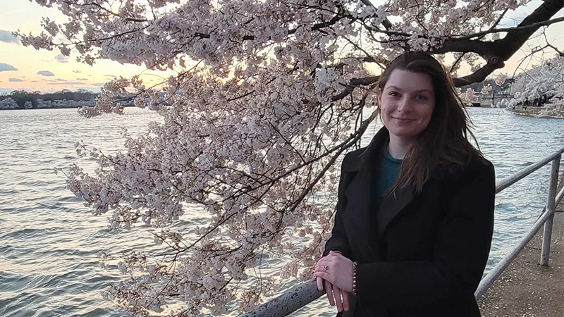 Raigan Lindquist smiling for a photo next to D.C.'s famous cherry blossom trees