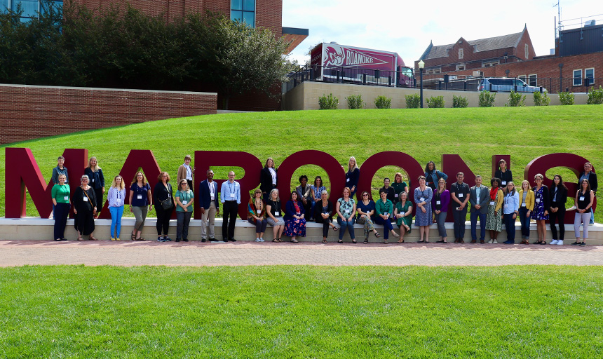 People pose for a photo next to a campus sign comprised of large letters that spell the word: Maroons