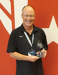 Man in a black shirt and lanyard holds an award in front of a red background