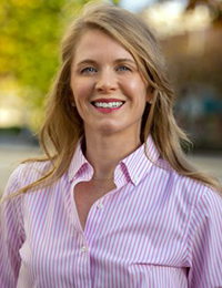 Headshot of a woman with long brown hair in a pink button-down shirt.