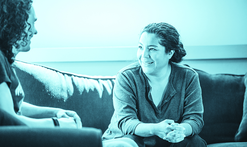 Blue-tinted photo of woman sitting on a couch talking to a student.