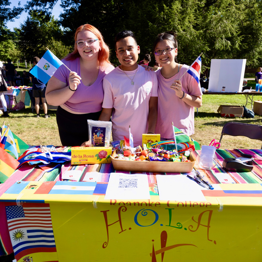 Three students smile for a photo at the HOLA booth of a campus activities fair