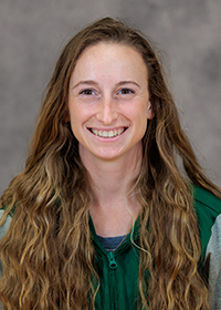 Young woman with long, wavy brown hair wearing a green windbreaker.