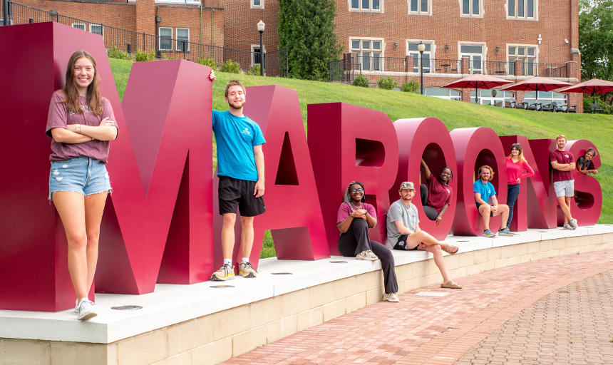 Students smile for a picture next to large letters that spell out the word: Maroons