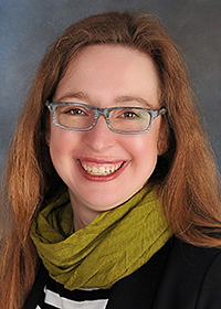 Woman in a brown sweater and glasses with a green scarf.