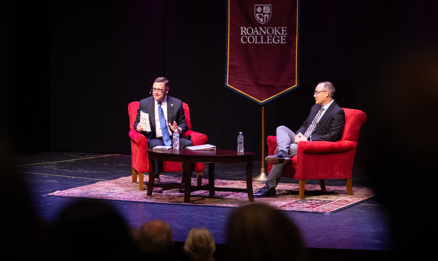 Two men address an audience while seated on a theater stage in Olin Hall at Roanoke College