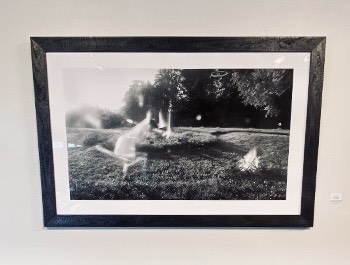 A black and white photograph of a blurred woman running around a fire pit.