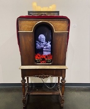 Artwork portrayed in an tall, vintage radio box, fake cherries, and fake candles.