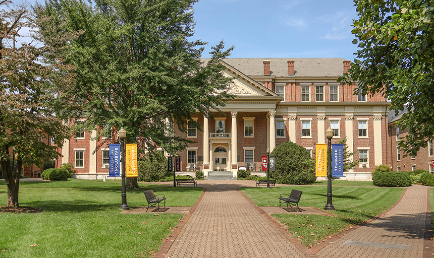 Large brick building with cream-colored columns, and a brick sidewalk leading up to it.