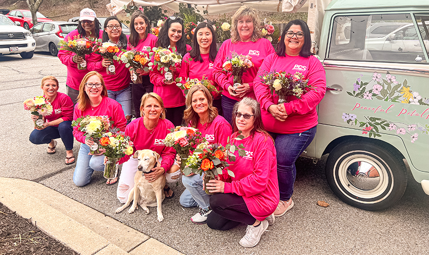 Group shot of 12 women all in bright pink PCS shirts and holding bouquets of flowers.