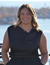 Woman in sleeveless blue dress standing with water in background