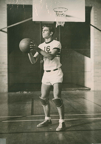 Black and white photo of a young man on the basketball court in a basketball uniform