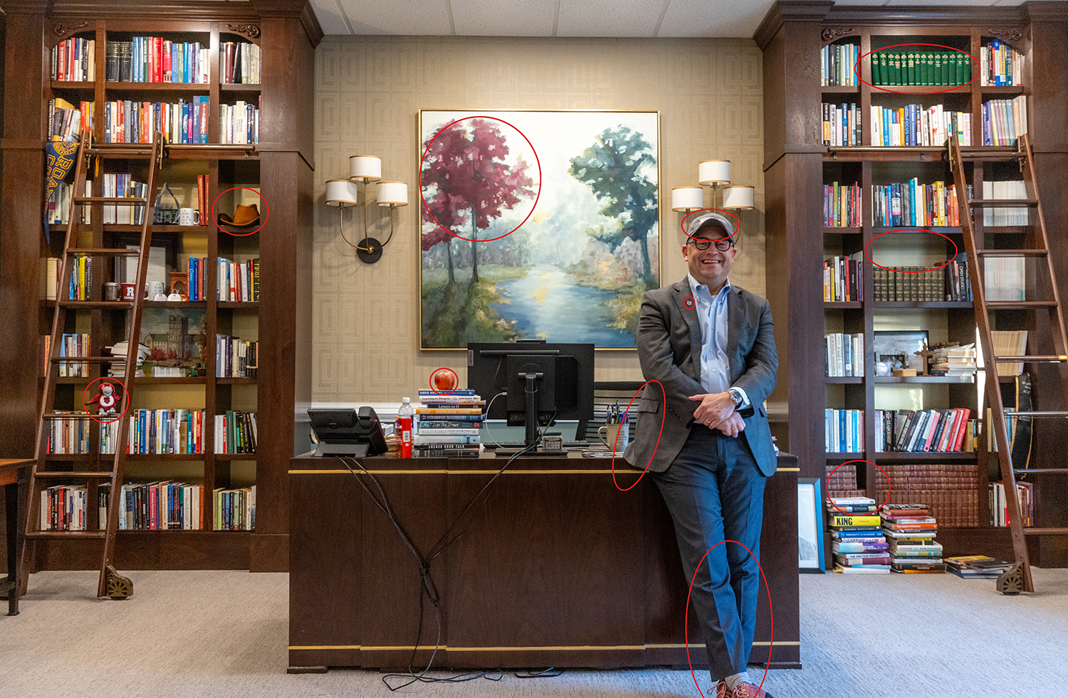 Photo of man in a suit leaning against a desk with bookshelves behind him.