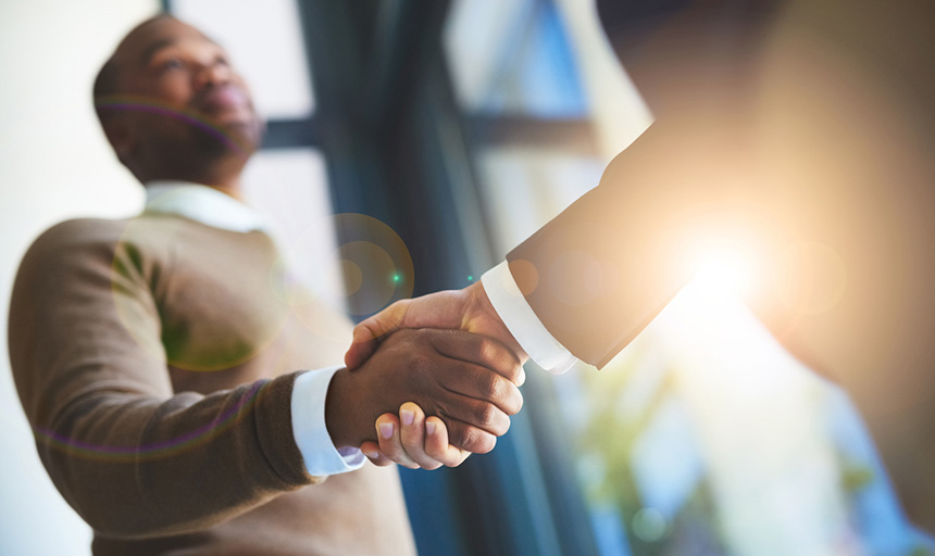 Two people shake hands with sun in background