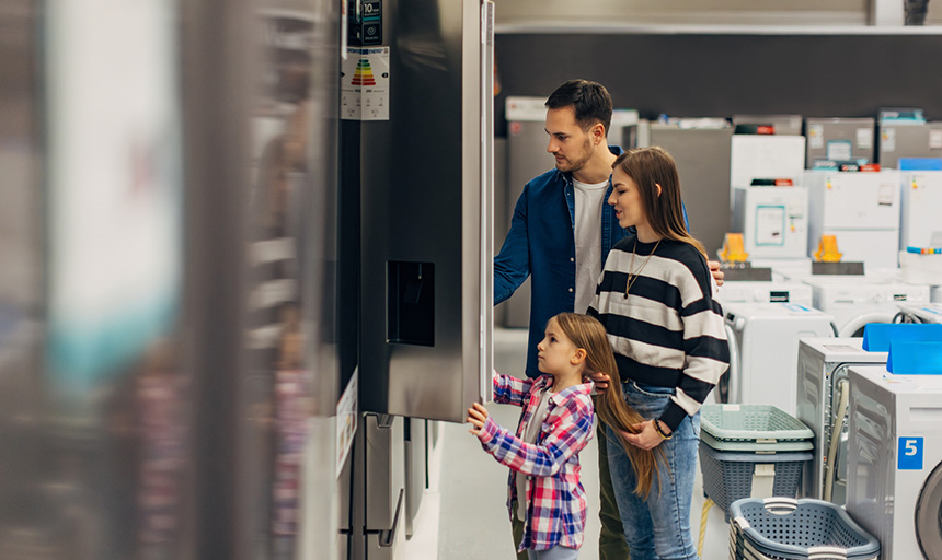 Two adults and a child look at line of refrigerators