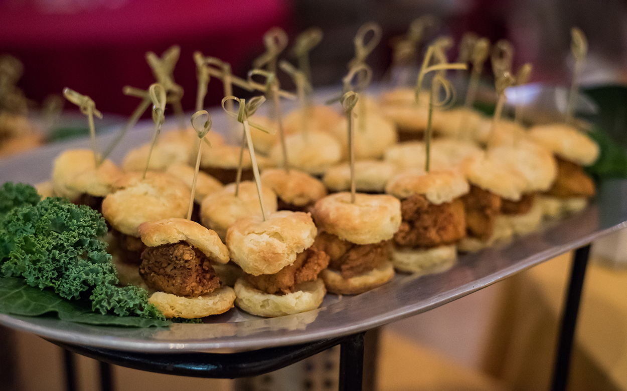 A platter of tiny biscuits with fried chicken on them.